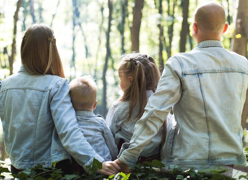man and woman holding hands together with boy and girl looking at green trees during day